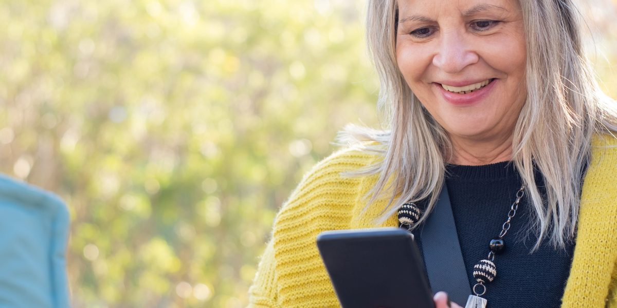A person comfortably viewing their smartphone screen outdoors under bright sunshine, highlighting the display's high peak brightness.