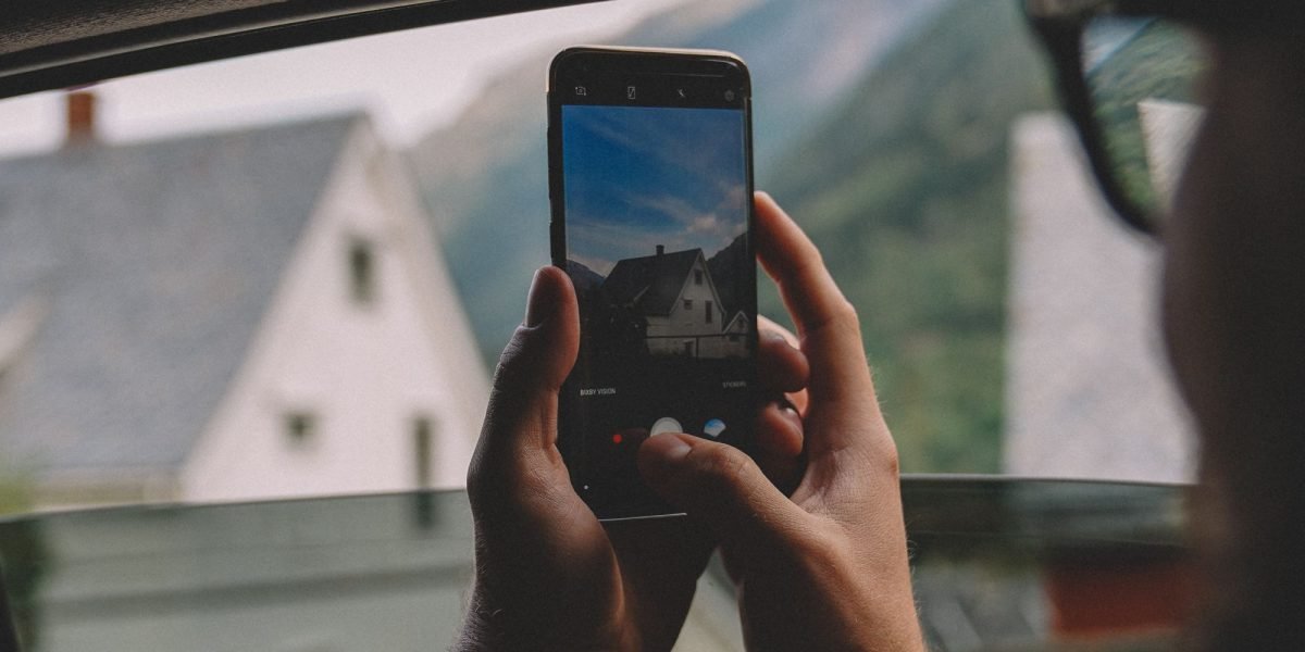 Someone actively capturing a moment or scenery with their smartphone camera in an outdoor setting, emphasizing the improved camera system.