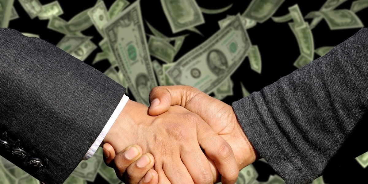 Two individuals engaged in a friendly negotiation or handshake, symbolizing successful bargaining for a tech purchase.